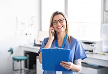 dental team member talking on the phone and holding a blue clipboard 