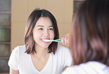 woman brushing her teeth in front of a mirror 