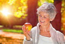 Woman with dental implants in West Palm Beach holding an apple