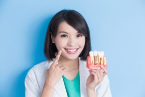 smiling woman holds jaw model with dental implants