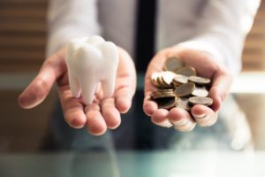 Hands holding pile of coins and model tooth